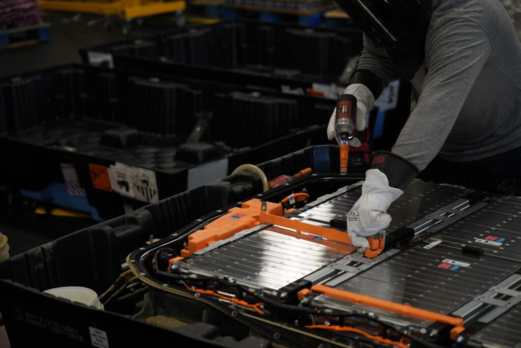 Technician disassembles an electric vehicle battery with an insulated drill and gloves